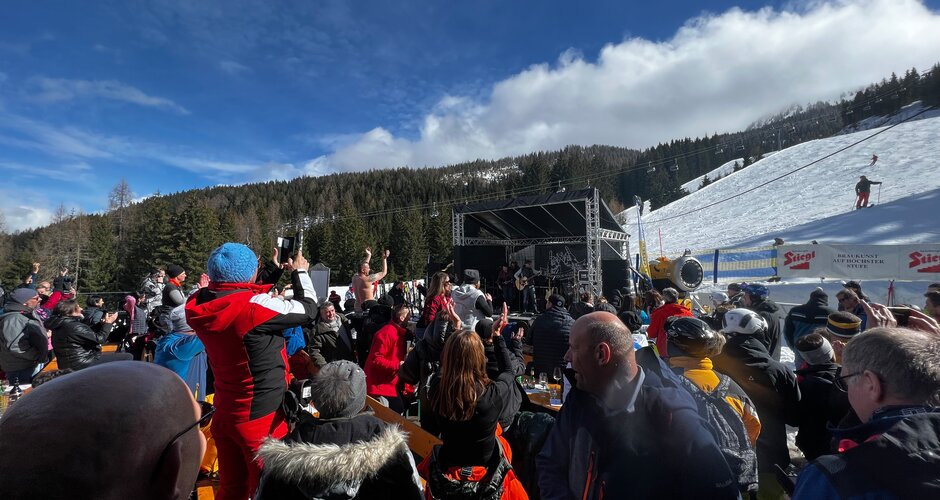 Many people in ski suits look at a small stage with musicians | © Hauser Kaibling