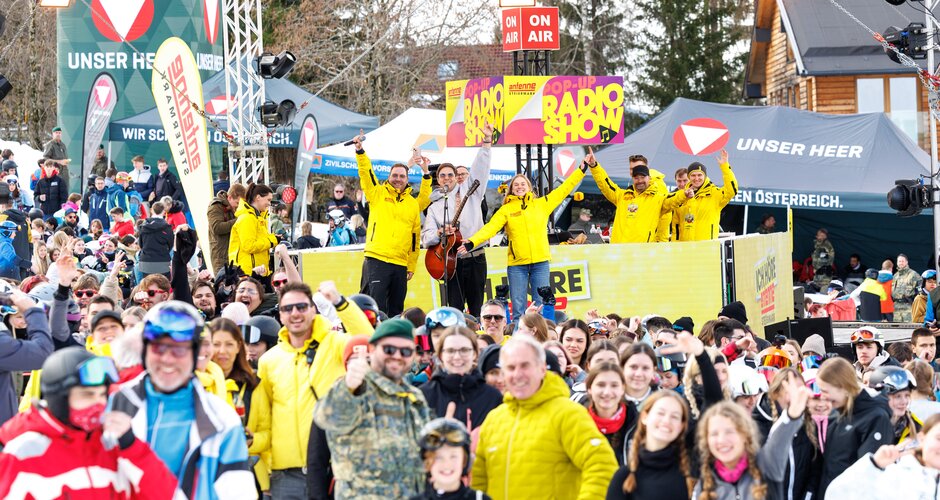 Crowd in front of stage with yellow-clad hosts at Antenne Snowday on the Planai. | © Erwin Scheriau