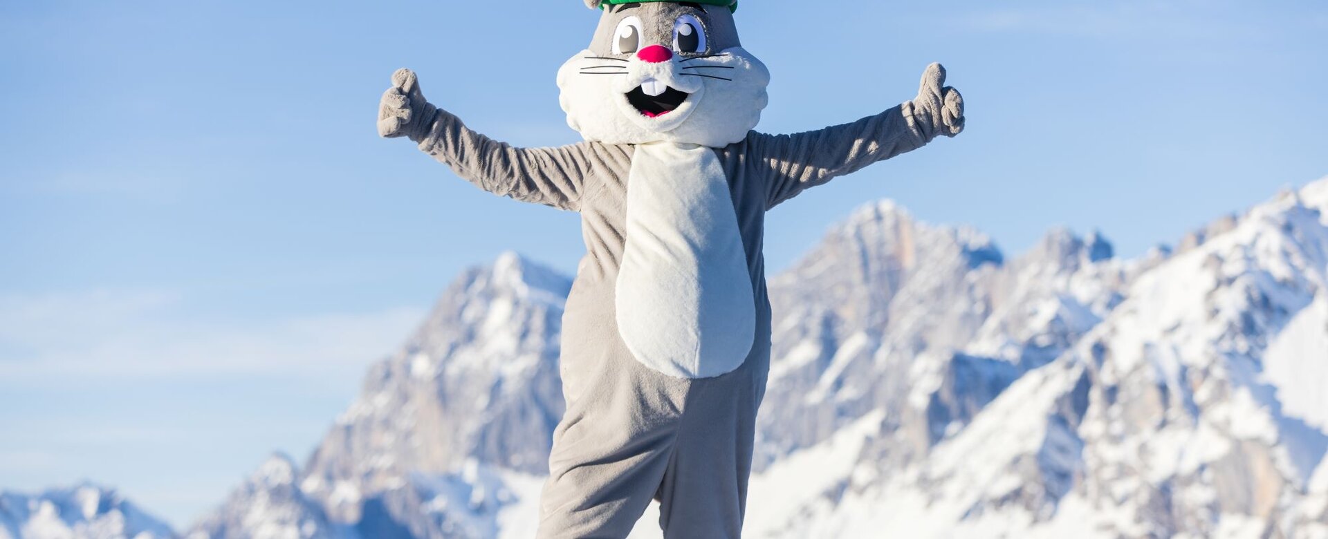 Hopsi the mascot is standing on the piste with both arms outstretched with his thumbs up | © Martin Huber