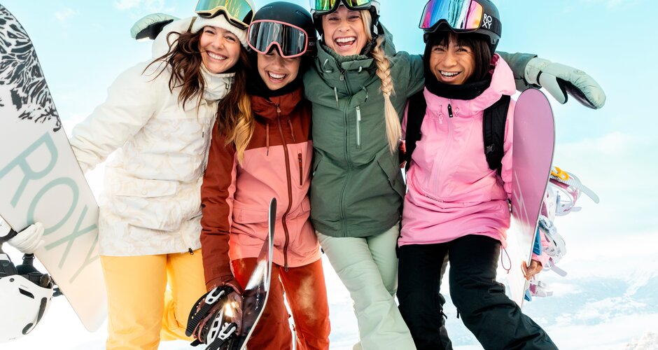 Four girls in ski gear hugging each other sideways and laughing into the camera | © QParks