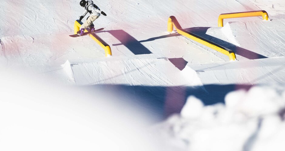Snowboarder glides over a metal railing in a snowpark | © Hannes Mautner