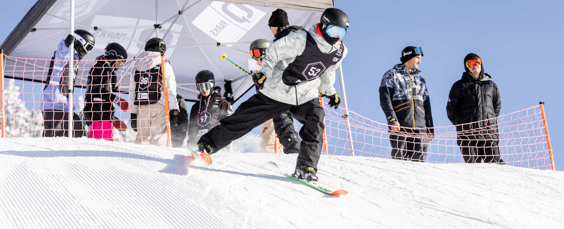 Freestyle skier skis away from the start and the next participants are already gathered under the tent at the start | © Hannes Mautner