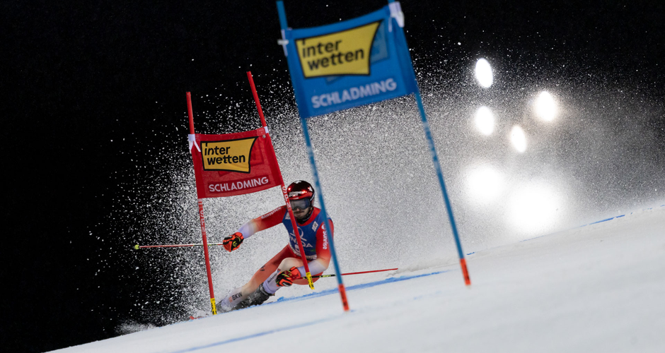 Skirennläufer passiert Riesentorlauf-Tore beim Nightrace in Schladming, Schneestaub fliegt im Scheinwerferlicht. | © Martin Huber