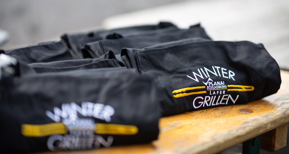 Several black aprons with “Wintergrillen Planai Schladming Lafer” logo on a table. | © Harald Steiner