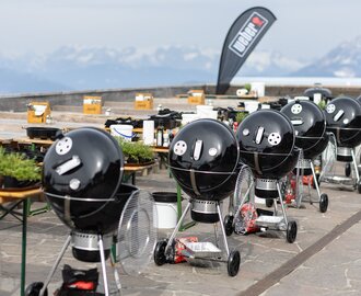 Reihe schwarzer Kugelgrills mit Zubehör auf einer Terrasse mit Blick auf Bergpanorama. | © Harald Steiner