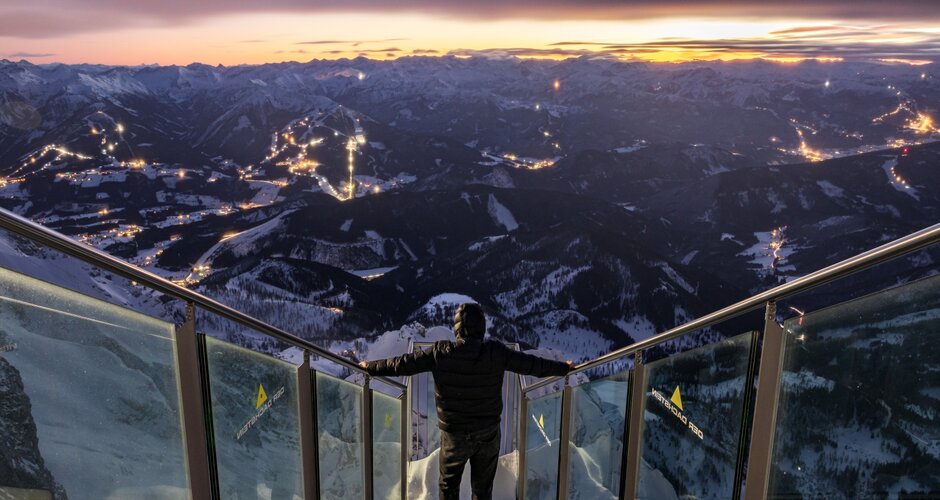Person steht auf der Aussichtsplattform am Dachstein und blickt auf das erleuchtete Tal bei Nacht | © Martin Huber