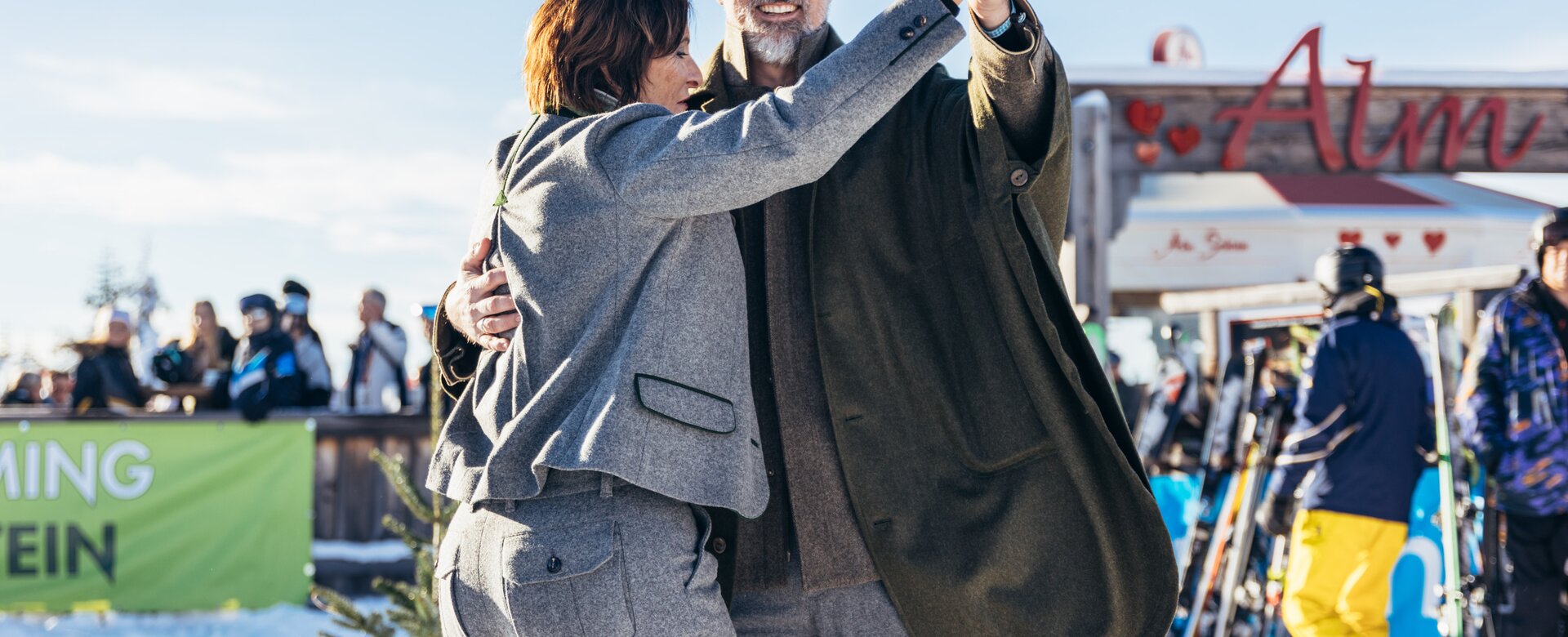 A man and woman dance in winter fashion in front of the Almbar on snowy Reiteralm mountain | © Gerald Grünwald