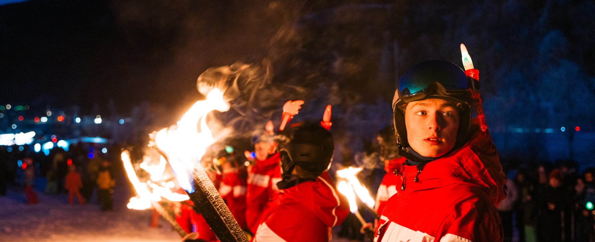 Junge Fackelträger in roter Skibekleidung stehen im Schnee bei nächtlicher Silvestershow bereit | © Gerald Grünwald