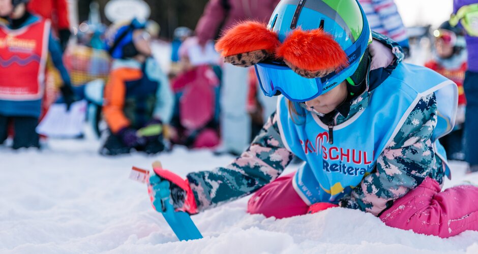 Ein Kind mit Schaufel kniet im Schnee und gräbt bei einer Schatzsuche auf der Reiteralm | © Gerald Grünwald