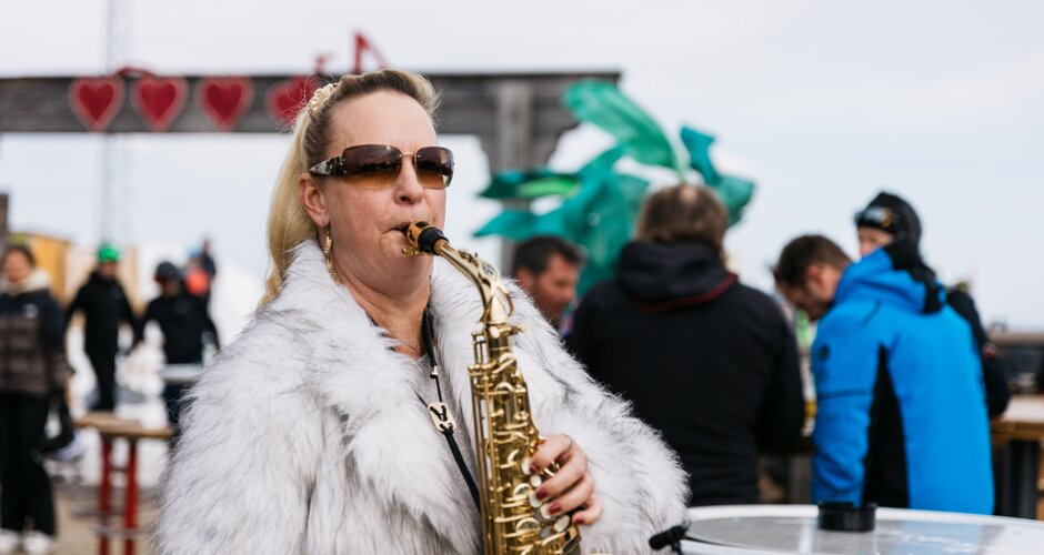 Woman in sunglasses and fur jacket plays saxophone at outdoor event on Reiteralm ski mountain | © Gerald Grünwald