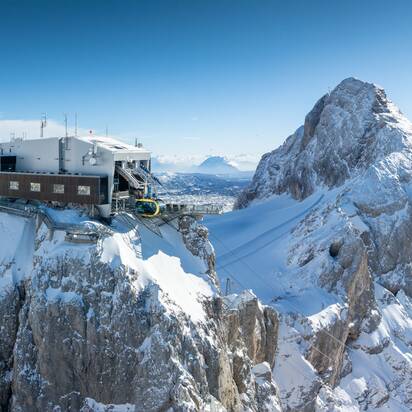 A modern mountain station with a cable car on a snow-covered peak, surrounded by an impressive mountain landscape. | © Josh Absenger