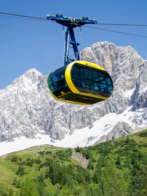 Yellow panorama gondola at Dachstein in front of glacier-covered cliffs and rugged alpine rocks