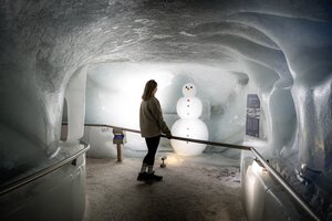 Besucherin betrachtet Schneemann aus Eis im Eispalast Dachstein, von Eiswänden umgeben. | © Juris Adventure