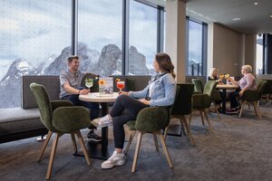 People enjoying drinks at tables with view of snow-covered mountains through panorama windows. | © Harald Steiner