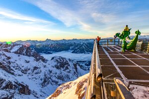 Snow-covered mountains, man on viewing platform, and green dragon figure at Dachstein. | © Renè Eduard Perhab