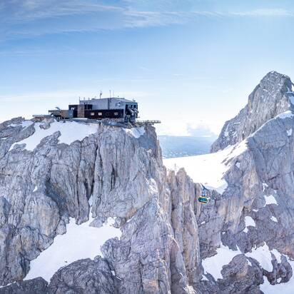Dachstein Gletscherbahn fährt zwischen schneebedeckten Felsgipfeln unter blauem Himmel. | © Josh Absenger