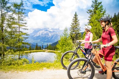 Two women with mountain bikes enjoy the view at a mountain lake | © Hauser Kaibling