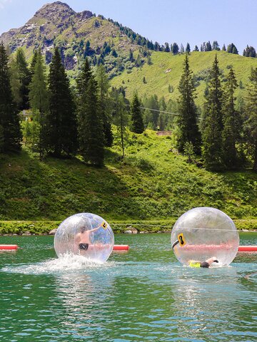 Two kids inside transparent zorbing balls on a lake with green mountains in the background. | © Hauser Kaibling