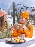 Two women with hats toasting drinks, plate of Kaiserschmarrn in the foreground. | © Bernhard Moser