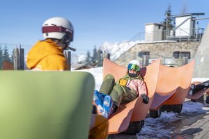 Two skiers relaxing in orange loungers at the Genussinsel in the snow. | © Bernhard Moser