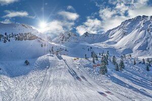 Ski slope with orange chairlifts, sun, and snowy mountains at Hauser Kaibling.