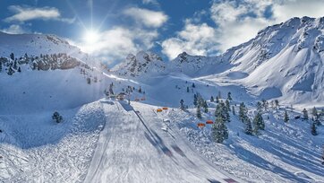 Ski slope with orange chairlifts, sun, and snowy mountains at Hauser Kaibling.