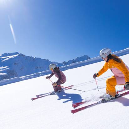 Two skiers ride in the sun on a groomed slope covered with fresh snow. | © Hauser Kaibling