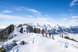 Winter hikers with snow-covered mountains and blue sky in the background. | © Gerald Oberreiter