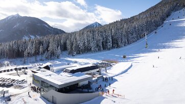 View of the valley station, skiers and gondolas, forest and mountains behind. | © Josh Absenger