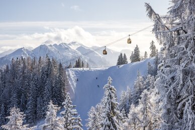 Snowy landscape with skiers, gondolas and mountains in the background. | © Martin Huber
