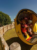 Two kids upside down in the yellow Moon Swing at Wilde Berg in Mautern, wooden fence and trees in background. | © Christine Höflehner