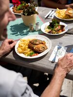 Grilled meat with fries, salad and drinks on wooden table in sunlight, served on a summer hut terrace on Planai mountain. | © Dietmar Körbler