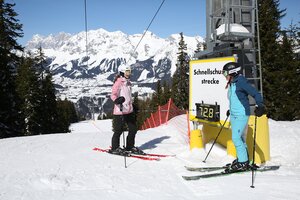 Two female skiers at the speed check course on Planai, one looking at the digital speed display showing 72.8 km/h. | © Herbert Raffalt