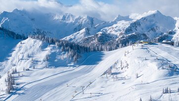 Snowy slopes with chairlifts and majestic alpine backdrop and blue sky. | © Josh Absenger