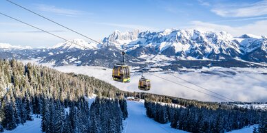 Two gondolas travel above snowy forests with majestic alpine mountains. | © Gerald Oberreiter