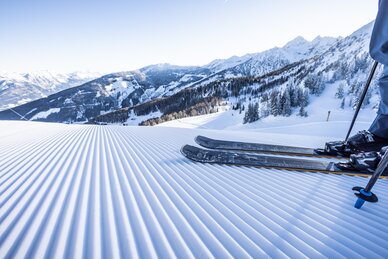 Skis on a freshly groomed slope with a snowy alpine landscape in the background. | © Mirja Geh