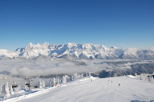 View of snowy slope, skiers, and impressive mountain panorama in the background.