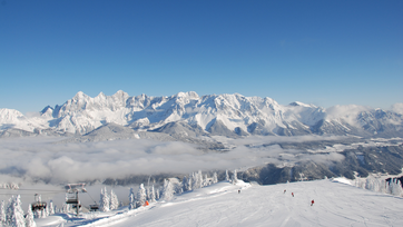 View of snowy slope, skiers, and impressive mountain panorama in the background.