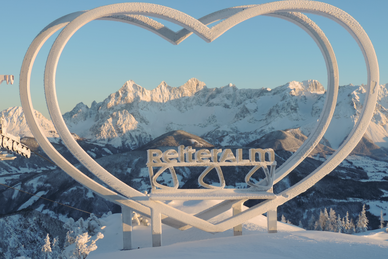 Steirerherz sculpture at Reiteralm with snow-covered Dachstein mountains in the background.