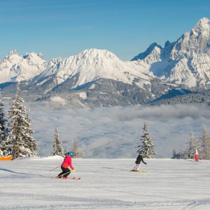 Two skiers on groomed slope at Reiteralm, with snow-covered Dachstein mountains behind. | © Lorenz Masser