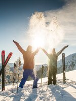 Two skiers toss snow in the air, sunlight, mountains, skis and poles in the snow. | © Lorenz Masser