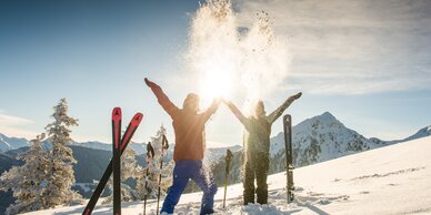 Two skiers toss snow in the air, sunlight, mountains, skis and poles in the snow. | © Lorenz Masser