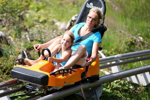 Mutter und Tochter sausen gemeinsam im Sommer mit dem Alpincoaster Rittisberg durch die Kurven, lachend in einem Schlitten. | © photo-austria