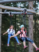 Zwei Kinder hängen gesichert in Gurten und schweben mit der Flyline durch den Wald am Rittisberg. | © Erlebnis Rittisberg