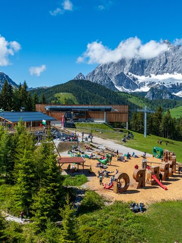 Weitläufiger Spielplatz mit Holzelementen, Rutschen und Kletterstrukturen vor einem Bergrestaurant und der Rittisberg-Seilbahn. | © Erlebnis Rittisberg