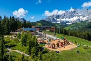 Spacious playground with wooden elements, slides, and climbing structures in front of a mountain restaurant and the Rittisberg cable car. | © Erlebnis Rittisberg