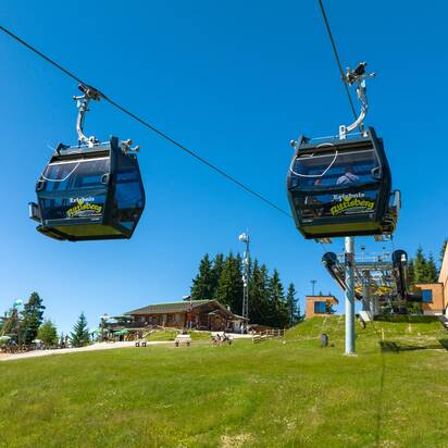 Two gondolas of the Rittisberg cable car reach the top station, with play area, huts and blue summer sky in the background. | © Rittisberg