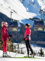 Zwei Frauen in Langlaufausrüstung stehen auf der Loipeund reden miteinander.