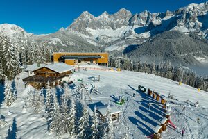 Luftaufnahme von der schneebedeckten Bergstation der Rittisbahn und einer Skihütte mit Spielplatz