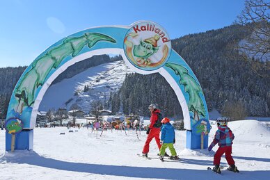 Drei Kinder auf Skiern unter dem bunten Eingangsbogen von Kaliland in Ramsau